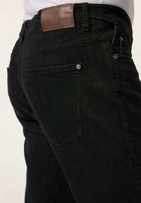 Schwarze Denim-Jeans mit einem braunen Leder-Aufnäher am Bündchen, Gesäßtaschen mit Metallnieten und einem Slim-Fit-Design.