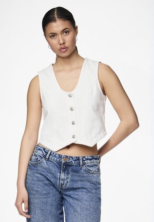 Hvit denim cropped vest med V-hals, prydet med sølvknapper og sømdetaljer, kombinert med falmede blå jeans.