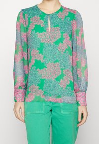 Blusa a maniche lunghe in tessuto trasparente verde con motivo floreale in rosa e blu. Presenta un collo a chiave e polsini delle maniche arricciati.