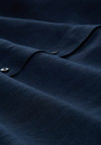 Textil de un bleu închis cu o textură moale, prezentând plieri netede și două butoane metalice. Materialul pare ușor și rezistent.