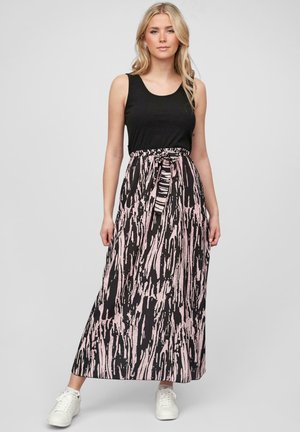 Jupe maxi longue, noire et rose à motifs, avec une taille cintrée et un détail de lien à l'avant, associée à un haut sans manches noir et des baskets blanches.