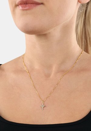 Goldene, gedrehte Kettenhalskette mit einem kleinen Kreuzanhänger, der einen zentralen Edelstein besitzt, getragen über einem schwarzen Hemd.