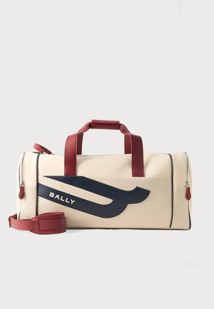 Cremefarbene und perforierte Ledertasche im Duffel-Stil mit dunkelblauem Logo, roten Griffen und verstellbarem Schultergurt, liegt flach auf hellem Hintergrund.