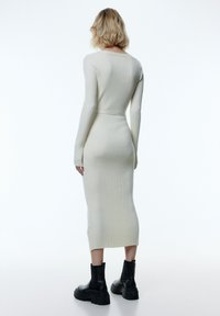 Rippendes, elfenbeinfarbenes Langarmkleid mit tailliertem Schnitt und Knielänge. Kombiniert mit klobigen schwarzen Knöchelstiefeln.