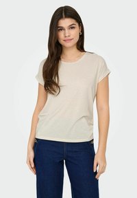 Beige gestreiftes T-Shirt mit kurzen Ärmeln, Rundhalsausschnitt und lockerer Passform. Kombiniert mit dunkelblauen Jeans mit goldenen Hardware-Akzenten.