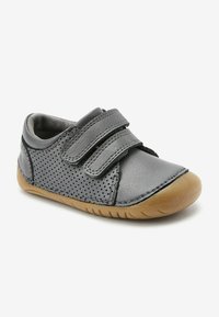 Grauer Lederschuh mit durchbrochener Gestaltung, zwei Klettverschlüssen, weicher Innenausstattung und Gummisohle. Abgerundete Spitze und minimale Nähdetails.