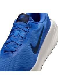 Niebieski but do biegania Nike z teksturowaną siateczką na górze, czarnym logo i białą podeszwą środkową z falistymi detalami. Widoczne płaskie sznurówki i wyściełany kołnierz.