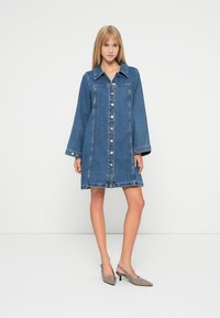 Denims kleiti ar pogām uz priekšu, izplestu apkakli un garām piedurknēm. Piemīt zila krāsa un kontrastējošas šuves, beidzas vidus augšstilba līmenī.