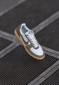 Nike tenisice s gornjim dijelom od bijele mrežice i smeđom kožom, bijelim vezicama i gumenim potplatom, s logotipom na jeziku i sa strane.
