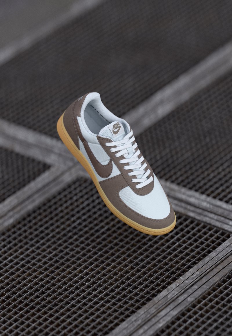 Nike tenisice s gornjim dijelom od bijele mrežice i smeđom kožom, bijelim vezicama i gumenim potplatom, s logotipom na jeziku i sa strane.