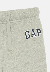 Harmaat collegehousut, joissa on elastinen vyötärö ja nauhat. Vasemmalla puolella on sininen "GAP" -logo brodeerattuna. Pehmeä pinta.
