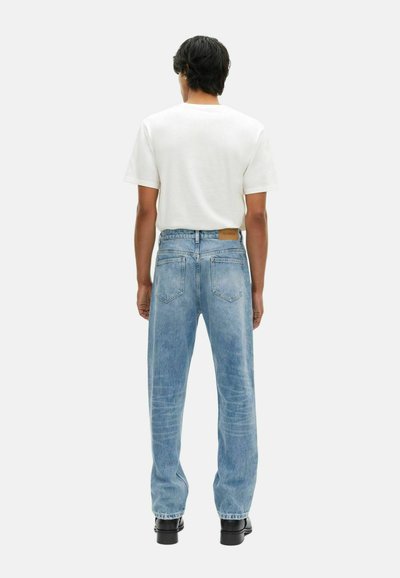 Lichtblauwe denim jeans met een losse pasvorm, vijf zakken en een bruine leren patch op de achterste tailleband. Gecombineerd met een witte t-shirt met korte mouwen.