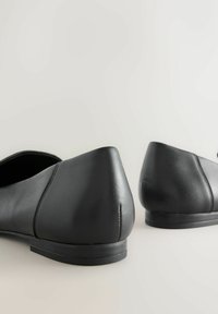 Čierne kožené balerínky s hladkou textúrou, špicatou špičkou, nízkym podpätkom a minimálnymi švami. Bočný pohľad ukazuje tvar obuvi.