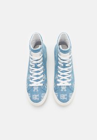 Sneakers alte progettate in denim blu chiaro, con un motivo a logo bianco, lacci bianchi e suola in gomma bianca. Dettaglio di tessuto testurizzato.