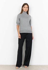 Pulover tricotat de culoare gri deschis, cu guler înalt și mâneci scurte, combinat cu pantaloni negri cu picior larg și pantofi cu toc deschis argintii. Textură simplă, croială lejeră.