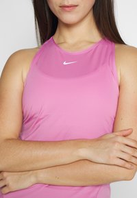 Top da allenamento fitted senza maniche di colore rosa chiaro, realizzato in tessuto traspirante. Presenta un piccolo logo Nike bianco sul colletto.