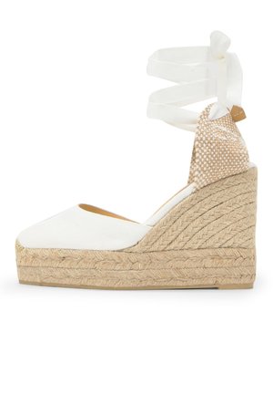 Alpargata de cuña blanca con puntera cerrada, plataforma de yute trenzado y cintas para atar en el tobillo de tela beige y blanca tejida.