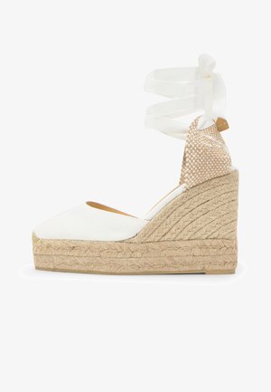 Alpargata de cuña blanca con puntera cerrada, plataforma de yute trenzado y cintas para atar en el tobillo de tela beige y blanca tejida.