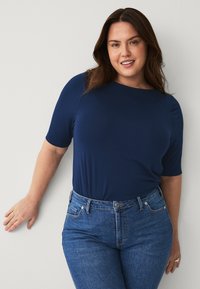 Dunkelblaues kurzärmliges Oberteil mit rundem Ausschnitt, kombiniert mit eng anliegenden hellen Jeans im klassischen Fünf-Taschen-Design.