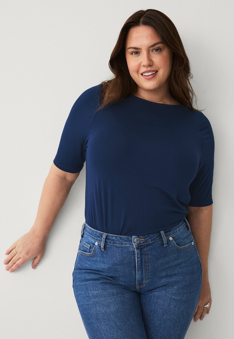 Dunkelblaues kurzärmliges Oberteil mit rundem Ausschnitt, kombiniert mit eng anliegenden hellen Jeans im klassischen Fünf-Taschen-Design.