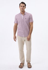 Kortærmet, knap-op skjorte med røde og hvide lodrette striber, parret med lyse beige bukser og brune sandaler. Enkel design, afslappet pasform.