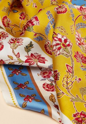 Sidenhalsduk med ett gult och vitt blommönster. Har röda, blå och gröna accenter, med intrikata detaljer och en mjuk textur.
