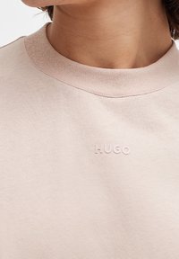 Bawełniewy sweter z okrągłym dekoltem w jasnoróżowym kolorze o teksturowanym wykończeniu. Posiada subtelnie wytłoczony logo "HUGO" na piersi.