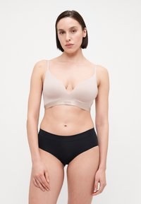 Lyse beige polstret bh med dyp V-utringning, tynne justerbare stropper og en glatt kant. Kombinert med svarte høyhårede truser.