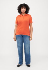 ORANJE gebreid poloshirt met korte mouwen, gestructureerd patroon en een kraag. Gepaard met blauwe recht-toe-rechstreeks jeans en zwarte platte schoenen.