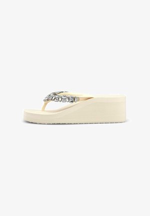 Sandalia flip-flop de cuña beige con suela gruesa y piedras brillantes rectangulares transparentes que decoran la tira en forma de T.