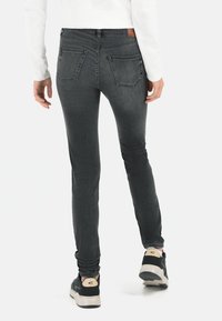 Skinny jeans in donkergrijs denim met achterzakken, hoge taille en een subtiele versleten textuur. Gecombineerd met zwarte sneakers met crême accenten.