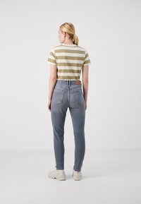 Ριγέ ελιά και κρεμ μπλούζα, ψηλόμεσα γκρίζα τζιν και μπεζ αθλητικά παπούτσια. Όψη από πίσω; Το τζιν έχει δύο πίσω τσέπες και ετικέτα μάρκας.