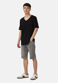 Czarny t-shirt z dekoltem w serek i krótkimi rękawami; szare szorty jeansowe; białe trampki z czarnymi akcentami; luźny krój. Prosty i stonowany design.