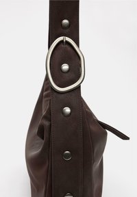 Borsa a spalla in pelle marrone con finitura testurizzata, caratterizzata da un grande accento in metallo argentato a forma circolare e dettagli a scatto in metallo sulla tracolla.