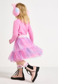 Maglietta lunga rosa, gonna di tulle a strati rosa e blu, cuffie rosa pelose e stivali combat rosa e neri con lacci.