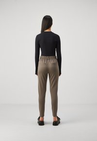 Black ribbed long-sleeve top paired with lightweight taupe pants featuring an elastic waistband and back pockets. Footwear with thick black soles.