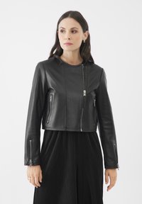 Giacca cropped in pelle nera con chiusura a zip, due tasche laterali e maniche lunghe con dettagli a zip sui polsini.