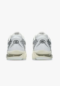 Un paio di scarpe da ginnastica bianche e grigie con ammortizzazione in gel, viste da dietro su uno sfondo bianco.