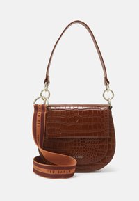 Brązowa torebka skórzana o fakturze krokodyla, w zaokrąglonym kształcie, z złotymi akcesoriami i odpinanym brązowym paskiem z napisem "TED BAKER" w kolorze pomarańczowym.