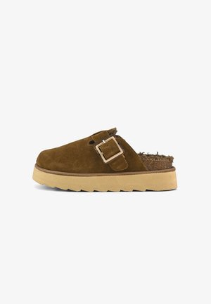 Ciabatte in scamosciato marrone, slip-on, con una larga fascia e una fibbia metallica rettangolare. Suola spessa e testurizzata beige che offre un contrasto. Interno foderato.