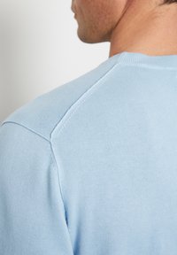 Maglione azzurro chiaro a maglia con scollatura rotonda, caratterizzato da una texture liscia e cuciture sulle spalle, visto da un'angolazione laterale.