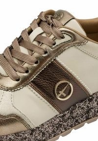 Sneaker, mille kreemi ja pronksise värvitooniga, millel on sünteetiline ja tekstureeritud nahk, silmatorkav logo ja täppidega tallad.