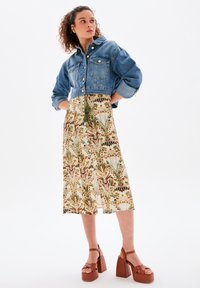 Jeansjacke mit verkürzten Ärmeln und zwei vorderen Taschen. Knielanges Kleid mit Blumenmuster in erdigen Farbtönen. Braune Plateausandalen runden das Outfit ab.