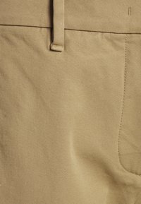 Lähikuva vaaleista housukankaista, jossa on nähtävillä vyölenkki, vyötärö ja sivutaskun ompelutiedot.