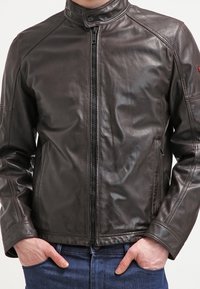 Mörkbrun läderjacka med hög krage, dragkedjestängning och två framfickor. Har en slät yta och en figurnära design.