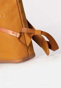 Hellbrauner Rucksack aus Leder mit glatter Oberfläche, ausgestattet mit einem verstellbaren Tragegurt und Akzentnähten. Enthält ein strukturiertes Mesh-Detail am Gurt.
