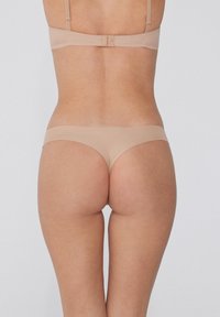 Beige-BH und String-Set, nahtloses Design, verstellbare Träger, weiche Textur, subtiler Glanz, minimaler Hardware, Rückansicht, die die Passform zeigt.