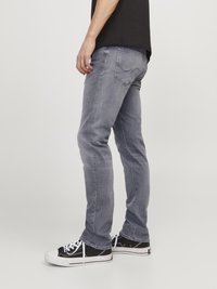 Graue Jeans aus Denim mit einem figurschmeichelnden Design, dezentem Used-Look und klassischem Fünf-Taschen-Stil. Kombiniert mit schwarz-weißen Sneakers.
