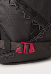Zwarte rugzak van textuurstof, met een roze plastic gesp, ingewikkelde stiksels langs de ritsen en een grijze riem.