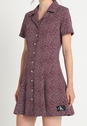 Short-sleeve maroon dress with white floral print, button-down front, collar, and black patch with "CK" logo near hem.